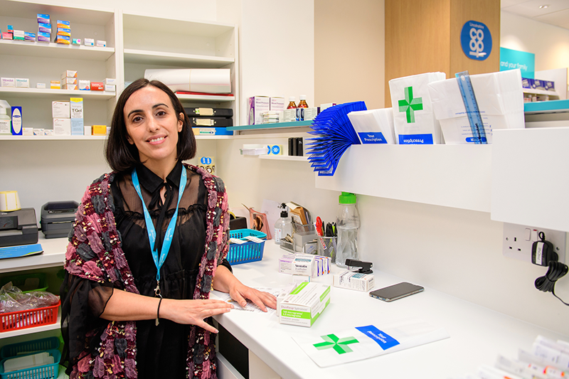 Dark haired woman wearing blue lanyard at a pharmacy desk