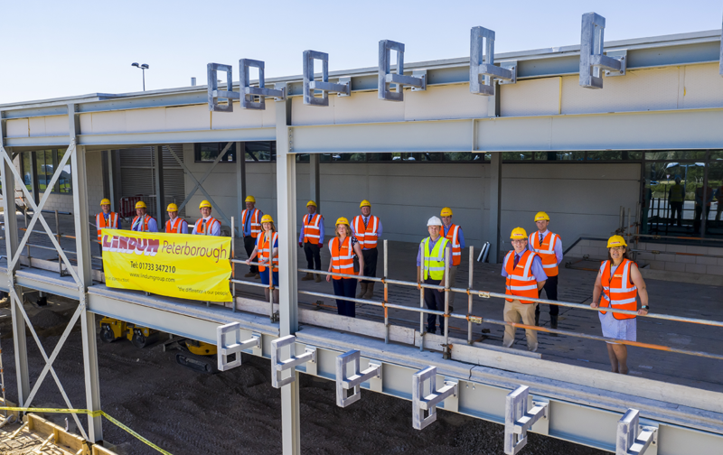 A group of people on a building site wearing hard hats and high visibility jackets with a large yellow banner and text Lindum Peterborough