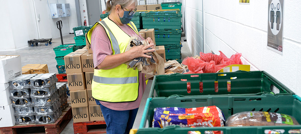 Woman in yellow high visibility jacket sorting food into green crates in warehouse unit