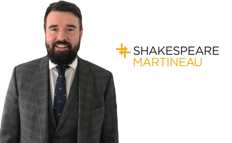 Calum Hanrahan, a man in suit and tie with dark hair and beard, next to Shakespeare Martineau logo in black and orange