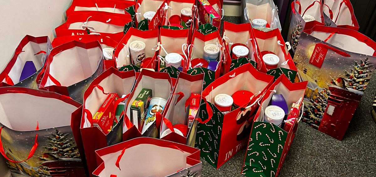 Over two dozen red Christmas gift bags with food items inside