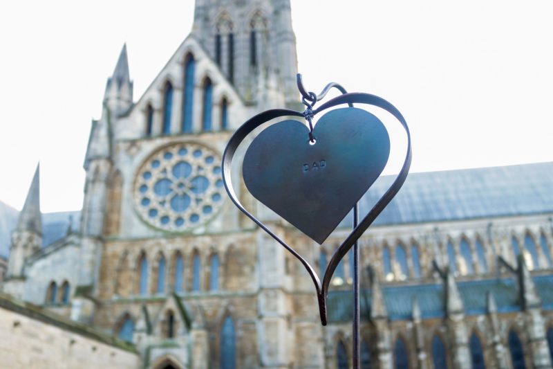 Iron wrought heart with engraved word 'dad' against backdrop of the Lincoln Cathedral