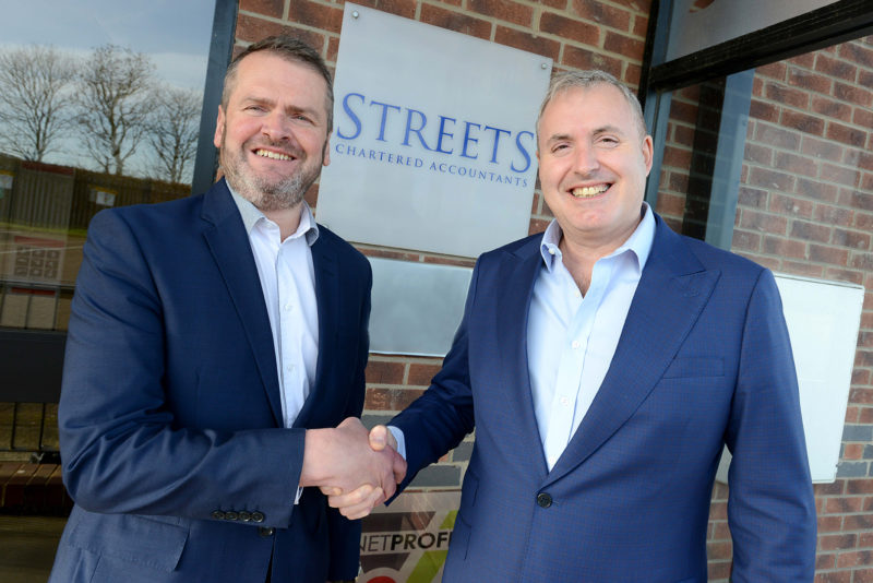 Two men in dark blue suits shaking hands outside of Streets Chartered Accountants office with sign