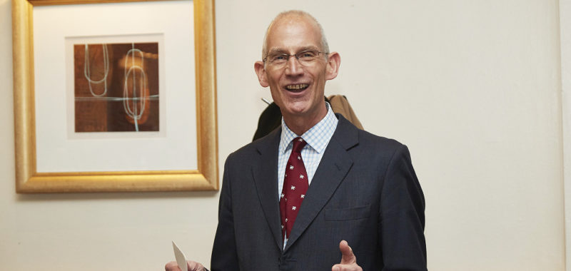 Julian Free CBE, a white male wearing dark suit and red tie with glasses