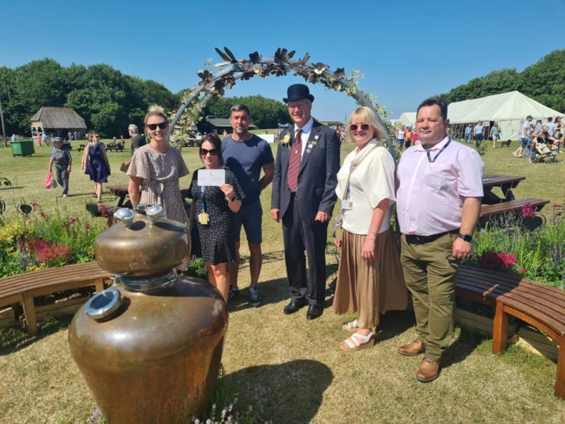 A group of men and women at the St Barnabas Hospice Sensory Garden at the Lincolnshire show. One woman is holding a certificate, and the group are surrounded by items in the garden.