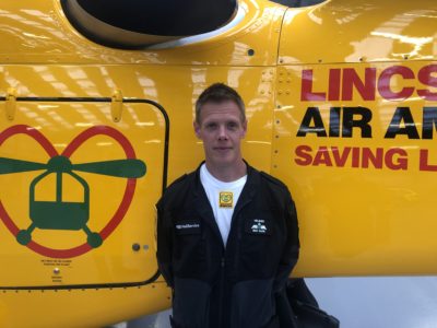A man wearing a black jacket standing in front of a yellow helecopter